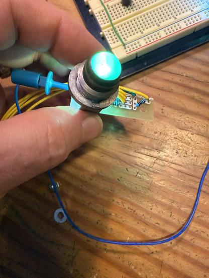 Holding a circuit board wiring up a multicolor LED that is sitting behind an antique dome light fixture, which is glowing a deep turquoise.