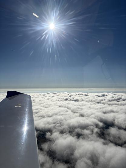 Blick aus dem Seitenfenster, unter uns sind Wolken und man sieht die hochstehende Sonne.