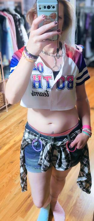 Alice's outfit for the event: short denim shorts, a pink and black plaid shirt tied around their waist,  a black sports bra, and a crop-top jersey in bisexual colors that reads "02 Both Teams".