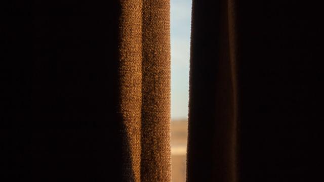 Burnt umber curtains in a dark room, parted slightly, catching the morning light from the world beyond.