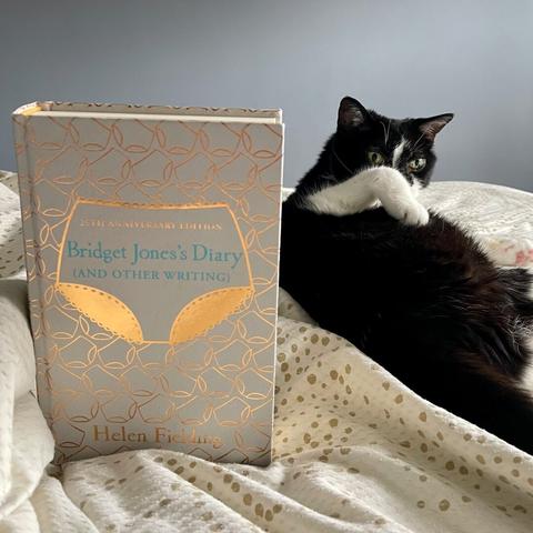 A cute black and white cat is shown next to a copy of Bridget Jones's Diary.