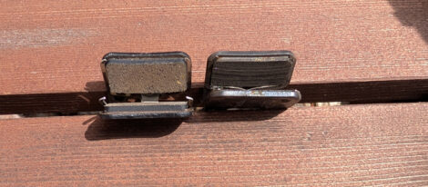 Zwei Sets Scheibenbremsbeläge für ein Fahrrad liegen auf der Kante zweier Holzbrettchen. Das eine Set hat nicht mehr so viel Belag, das andere ist nagelneu.