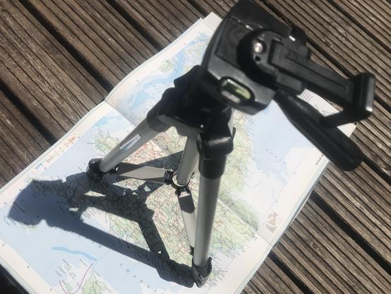 A small tripod stands on an atlas, spread open to reveal a map of the UK.