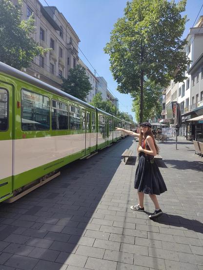 Aada steht neben einer grün/weißen alten Tram in der Breiten Straße und zeigt auf diese.