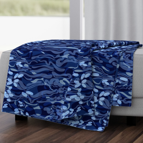 A mock-up of how the abstracted repeat pattern depicting the surface of moving water would look as printed on fabric for a blanket on a piece of living room furniture. The fabric is printed in tones of cobalt blue, with plenty of cascading lozenges in pale blue.
