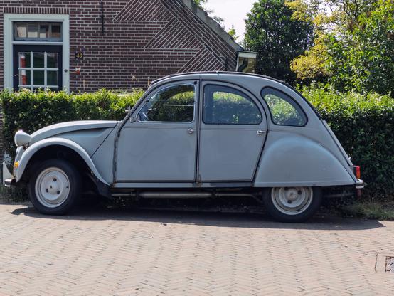 A vintage grey car parked beside a brick house in Huizen, Netherlands.