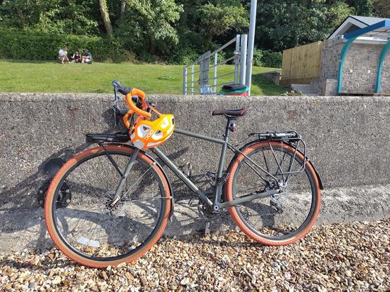 a green bicycle with orange handlebars and tyres is parked against a sea wall on a shingle beach