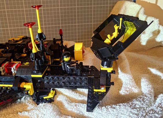 A small Blacktron Lego build of the "Instigator" is successfully docked to a bigger one, the "Renegade" from 2025. Its pilot minifig is sitting inside with a smile.