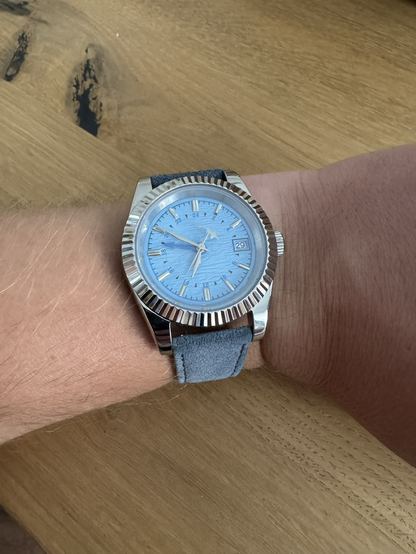 A wrist watch with a wavy blue dial. The second hands balance is a shark „swimming“ circles. Now on a blue leather strap