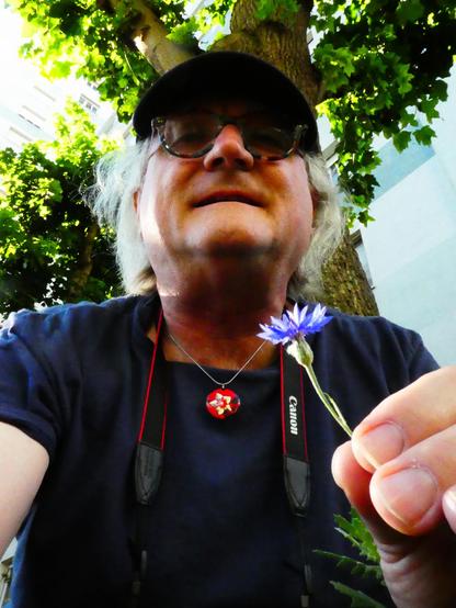 Reinhard, vor einem Baum am Boden sitzend, untersucht eine schöne Kornblume.