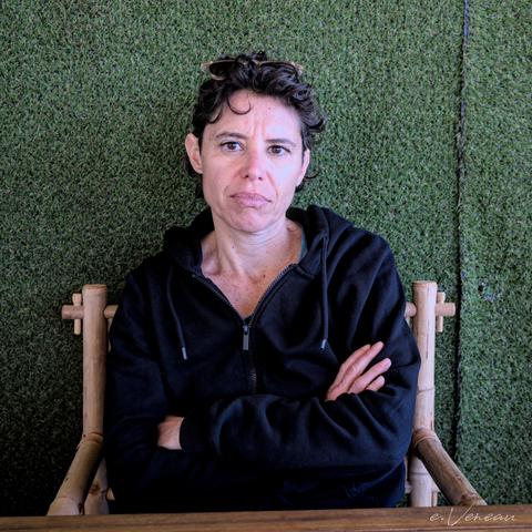 Portrait of a woman wearing a black top, seated, arms folded, facing front.