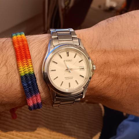 Seiko SBQK079 [JDM] Perpetual Calender with an off white dial and baton indices, with minimal lume. It also has a date complication. Steel case with a steel bracelet. On the same wrist is a rainbow band. The time shown is 11:14:08 [23:14:08]. The date is the 29th.