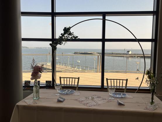 the brides’ table and chairs, in front of a window showing a view of the waterfront