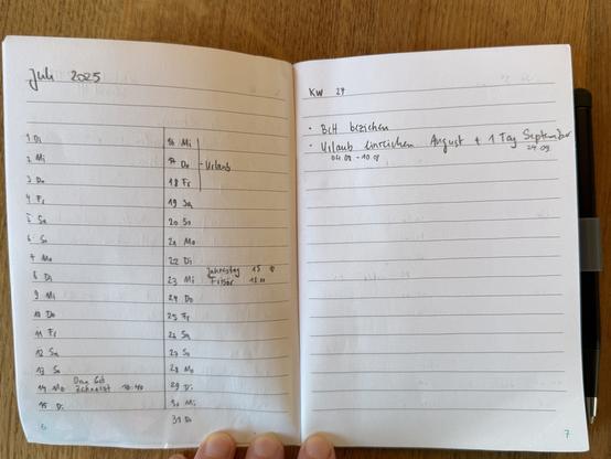 Double page in a A6 sized notebook. Left pages header is “Juli 2025”. I halved the page with a line in the middle and wrote in the left column the dates and corresponding abbreviated weekday in German “ 1 Di” to “15 Di” and in the right column “16 Mi” to “31 Di” top to bottom. There are some entries on “14 Mo” (grandma’s birthday and a dentist appointment) I have three days off “16 Mi” to “18 Fr”. My partner and I celebrate our anniversary on “23 Mi” and I also plan to go to the hairdresser. 

On the right page is “KW 27” written on top indicating the current week and number. 
It’s my to do list. I have to change the bedding and I have to ask for some days off in August and September. 

The book lays on a wooden table. On the left is a blue pen visible. On the bottom three of my white fingers are holding the book open.