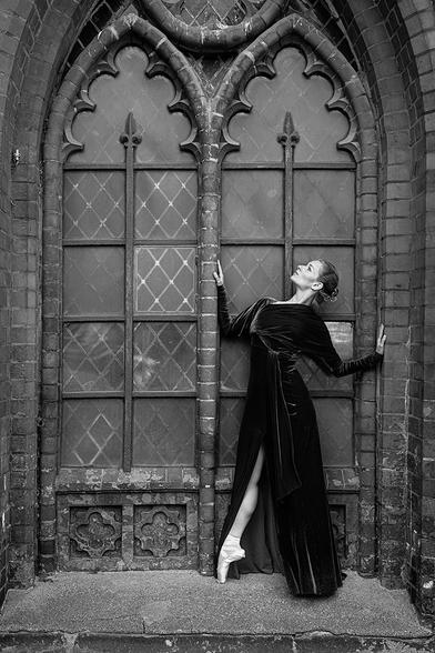 Ballettänzerin auf Spitze stehend draußen vor einem alten Kirchenfenster
