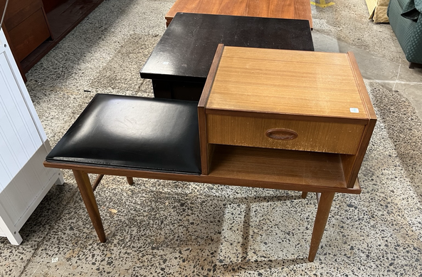 A low bench with a vinyl covered seat on one side, a small table with a drawer and an open space on the other