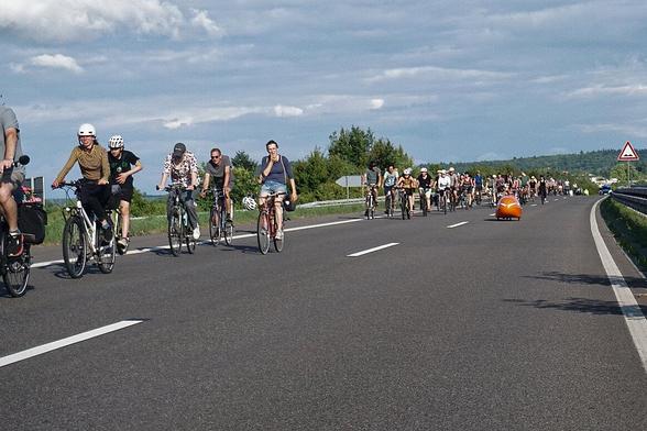 Fahrraddemo auf dem rechten Fahrstreifen einer autobahnähnlich ausgebauten Kraftfahrstraße. Der linke Fahrstreifen ist – bis auf ein Velomobil – frei.