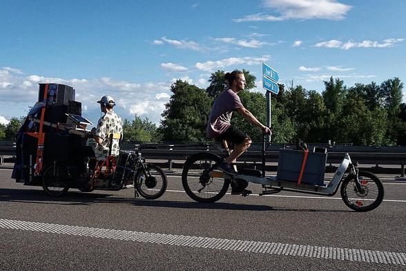 Ein Lastenrad mit Anhänger und Soundanlage. Auf dem Anhänger sitzt ein DJ.