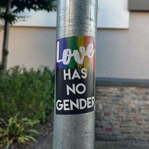 A rainbow sticker on a sign post that reads, "Love has no gender."