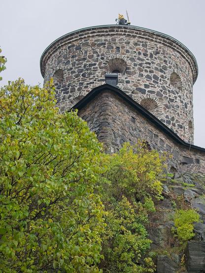 Vi står nästan under Skansen Lejonet i Göteborg och tittar upp längs fasaden. Ett grönskande träd täcker en del av bilden.