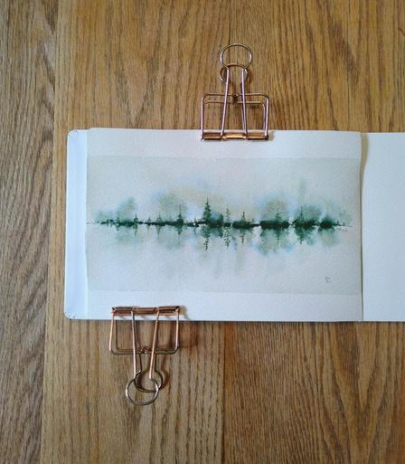 This is a Reflective Atmospheric Watercolor Landscape Painting in landscape orientation in an A5 sketchbook. The rectangular boundaries and smaller sized evergreen trees give a panoramic feel. The largest tree (and its reflection) is 1/3 of the total height of the painting. I used Daniel Smith Cascade Green for this experimental piece for its granulation and color splitting; it's made with raw sienna and phthalocyanine blue. With masstone of a dark yellow green at the tree line, some of the medium values are also yellow green with a distinct blue edge. Elsewhere medium and light values of raw sienna are visible.  The lightest value is minty green. The trees are tallest in the center and shortest on the sides. The overall feeling is the mistiness in the early morning.