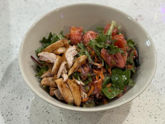 A serving bowl full of fresh vegetables, carrots, chard, radishes, scallions, collards, tomatoes, onions and mesclun greens. It was tossed in a blueberry jam and mustard vinegrette and topped with some roasted chicken.