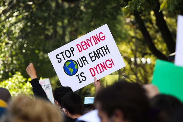 A placard held up during a demonstration, reading "stop denying our planet is dying.