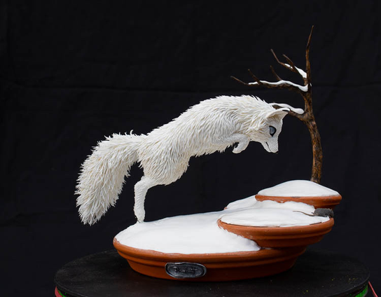 A sculpture of a white fox jumping and hovering in mid-air. Its focused on a point in the front of him, under the snow.