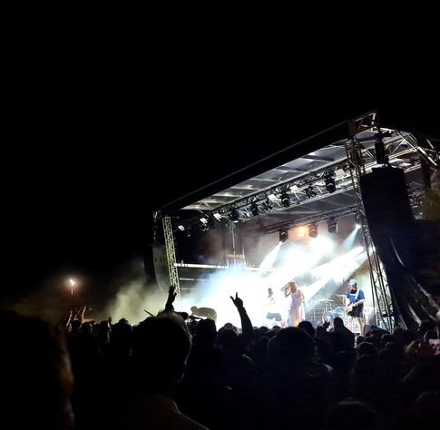 Photo d'une scène de festival de nuit. Les spot mettent en lumières le chanteur en robe rose devant un public chaud comme la braise