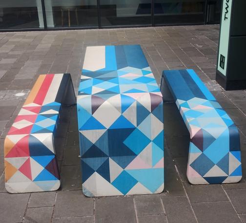 Plastic table and benches painted in overlapping, geometric shapes in shades of blue, grey, red and orange
