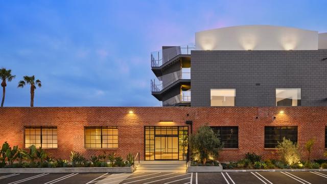 Ansicht der neuen Apple Music Studios in Los Angeles mit roter Backsteinfront, großen Sprossenfenstern und modernen grauen Backsteinen mit gewundenen Außentreppen im Hintergrund. Foto (c) Apple.