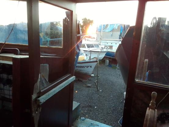 View from wheelhouse, sun setting, in. The foreground the bow of a possibly abandoned boat with the name Woodstock