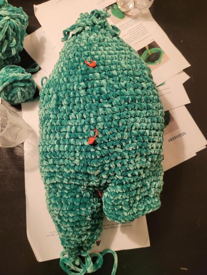 Virkat monster i grönt velour aktigt garn stoppat med vadd utom ena benen som ska virkas klart.