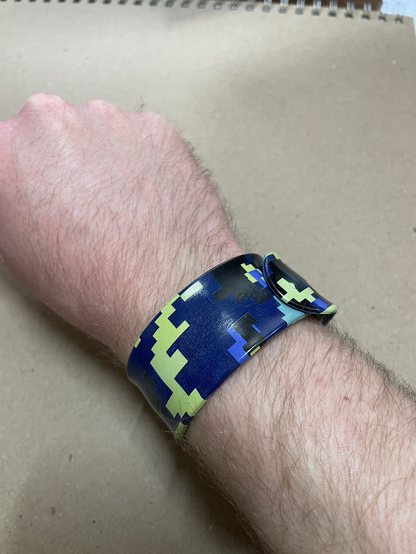A man’s arm wearing a camo colored slap bracelet that is also a ruler!