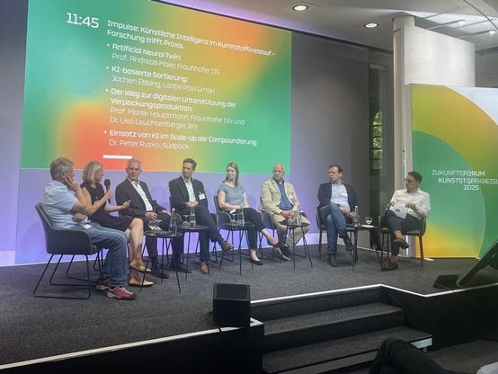 Die Teilnehmenden der Podiumsdiskussion sitzen im Halbkreis auf der Bühne, vertieft in eine Diskussion