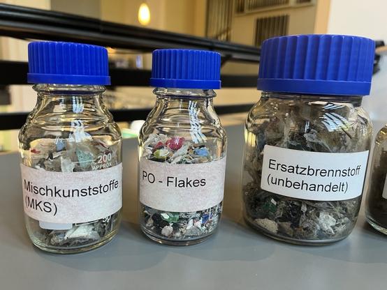 Drei kleine Fläschchen mit buntem Inhalt. Sie tragen Etiketten, die erklären, um welche Art von Kunststoff es sich handelt.