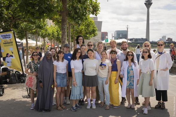 Gruppe von Menschen vor dem Rheinturm Düsseldorf während des Soapbox Science Events. Einige tragen weiße Laborkittel.