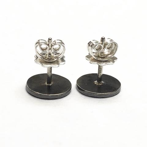 A pair of silver earrings featuring a decorative structured design. The earrings are stud style, with a circular base and intricate detailing on the top part.