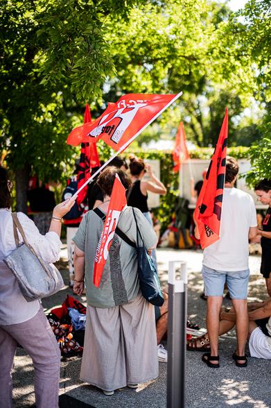 Une manifestante de dos avec son drapeau FO, un autre drapeau FO flotte au dessus d'elle. Et une personne avec un drapeau SUD Solidaire et à côté