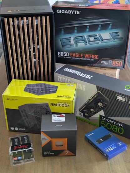 Picture of a stack of boxes containing PC parts, next to it a PC case with a wooden front mesh.
Thr GPU is an RTX 5080, the CPU is a Ryzen 7800X3D.