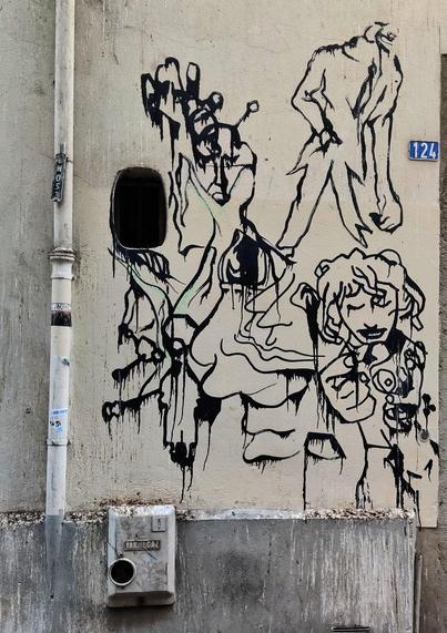 Un graffiti abstracto en una calle de Chambéry. Se distinguen caras y algunas figuras humanas. El graffiti es negro sobre una pared blanca.