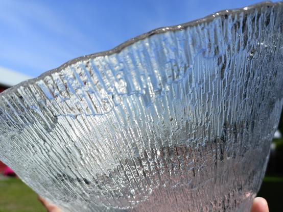Cristal bowl with a design inspired by Arctic landscapes is seen from the side while holding it against the blue sky.