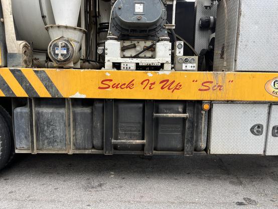 a sign on a hydraulic excavation truck that says in stylized text “Suck It Up ‘Sir’ “

the truck has grey and black tanks and fittings, the sign is on an orange safety strip