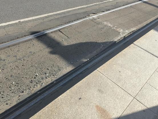 Light rail embedded into a road. The Road has expanded upwards and is visibility bulging. There is paint scratches ontop of the bulge.
Asphalt debris is visible.