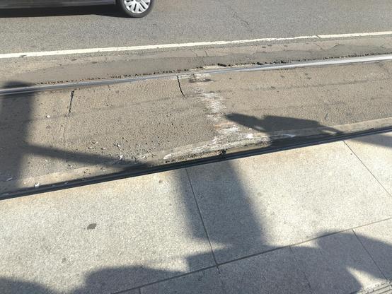 Light rail embedded into a road. The Road has expanded upwards and is visibility bulging. There is paint scratches ontop of the bulge.