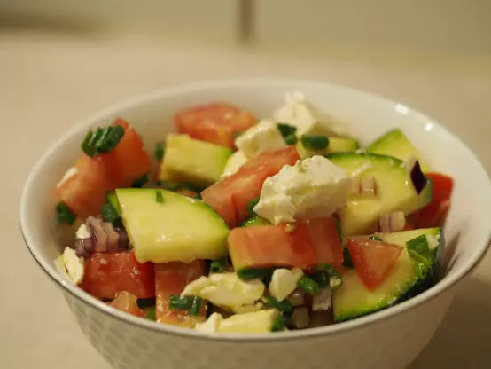 Eine kleine Schüssel gefüllt mit einem Salat aus rohen Zucchini, Tomaten, und Hirtenkäse