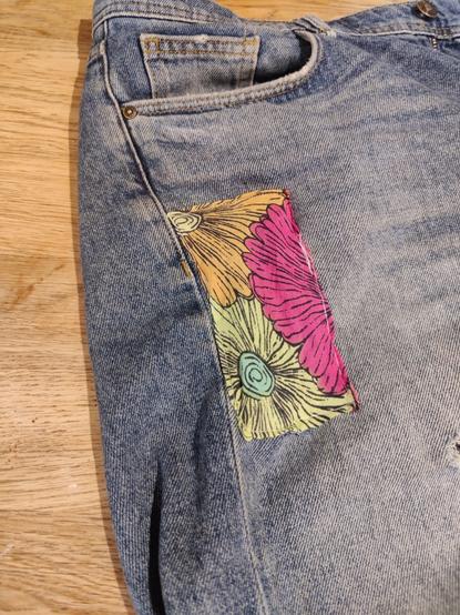Vue rapprochée sur un short en jean bleu un peu délavé, avec un patch de tissu fleuri rouge vert et jaune.
La couture reste un peu approximative !