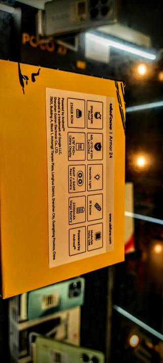 The photograph shows a yellow box with a label on it. The label contains various icons and text, providing information about the product inside. The text on the label reads:

"Powered by Android™"
"256GB ROM"
"120Hz FHD+ Display"
"6.78" In-Plane Switching (IPS) Type 9EK"
"MIL-STD-810H Certified"
"64MP Rear Camera + 64MP Front Camera"
"22000mAh Mega Battery"
"IR Blaster"
"Versatile Light"
"Powered by Android™"
"MediaTek Helio G96"
"Armor 24"

The label also includes the address "7B01, Building A, Block 1, Anhongji Tiyu, Anhongjia Plaza, Longhua District, Shenzhen City, Guangdong Province, China" and the website "www.ulefone.com." The box is placed on a reflective surface, and in the background, there are blurred images of other boxes and a sign with the text "POCO."

 Ovis2-8B

🌱 Energy used: 1.862 Wh