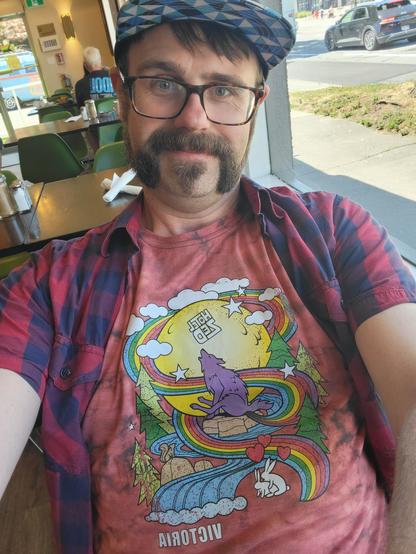 A selfie of me wearing a tie dye shirt from the Hotel Zed where we are staying. It features a graphic applied over the tie dye of a purple fox with a magical rainbow coming out of its ass and spiraling around the moon.