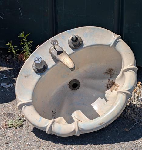 a whimsical face in the form of an old scalloped-edge porcelain sink with missing/mismatched chrome fittings
